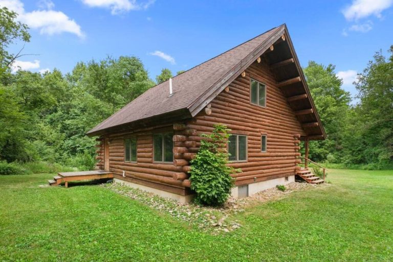 Two-story log cabin exterior surrounded by trees in Evart, Michigan — Coyote Fire Retreat, hosted by Roam