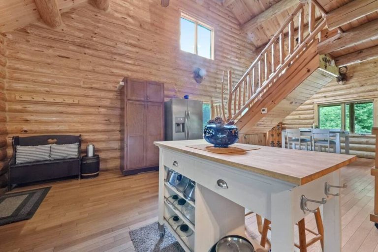 Great room with kitchen island and log staircase in Evart, Michigan — Coyote Fire Retreat, hosted by Roam