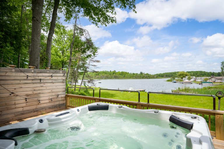 Deck hot tub with lake view in Reed City, Michigan house — Lakeside Lodge Retreat, hosted by Roam