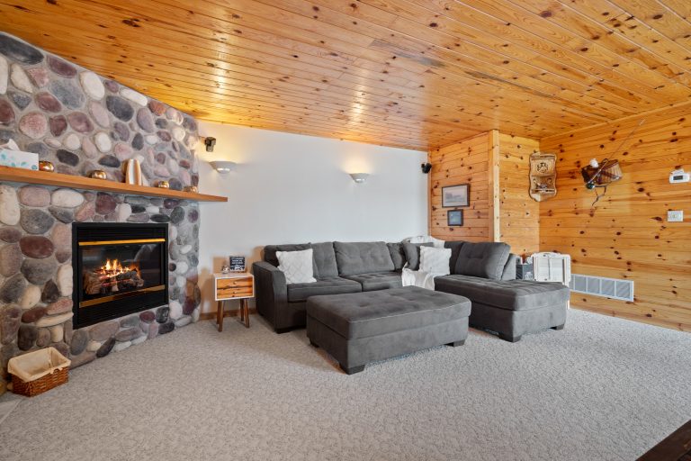 Living room with stone fireplace and sectional in Reed City, Michigan house — Lakeside Lodge Retreat, hosted by Roam