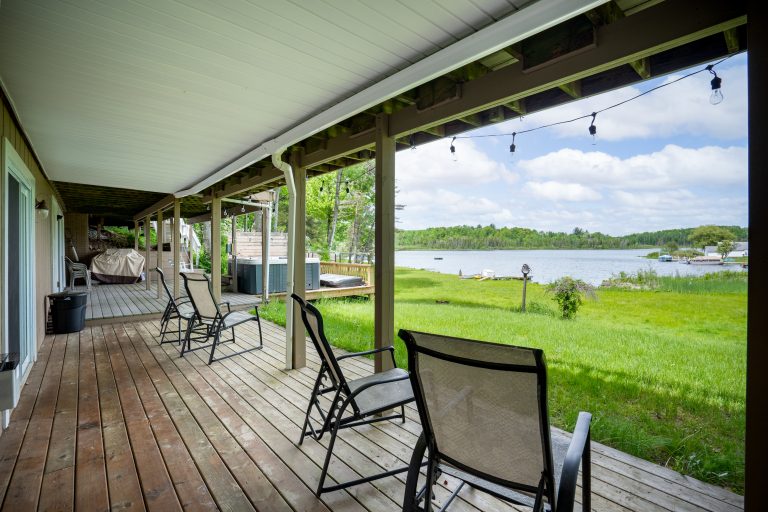 Covered deck with lake view and seating in Reed City, Michigan house — Lakeside Lodge Retreat, hosted by Roam