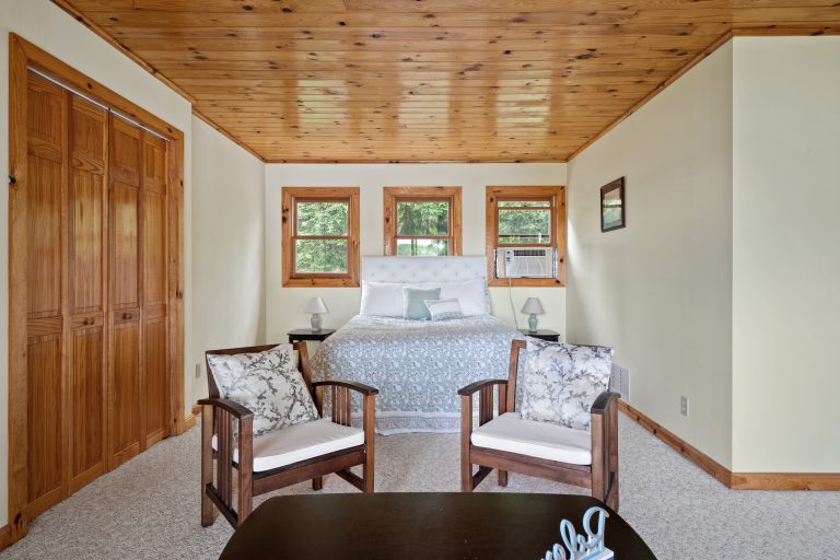 Bedroom with tufted headboard and wood ceiling in Reed City, Michigan house — Lakeside Lodge Retreat, hosted by Roam