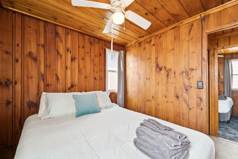 Wood-paneled bedroom with queen bed and doorway view Cabin in Oscoda, Michigan — Barefoot Beach Cabin #4, hosted by Roam