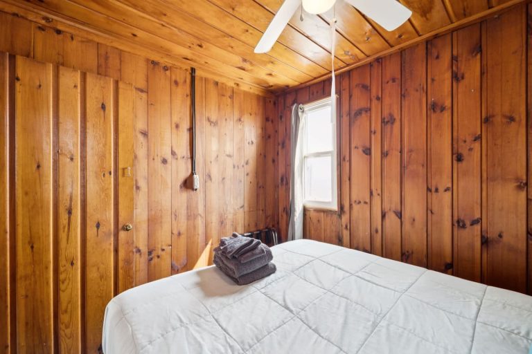Wood-paneled bedroom with folded towels Cabin in Oscoda, Michigan — Barefoot Beach Cabin #4, hosted by Roam