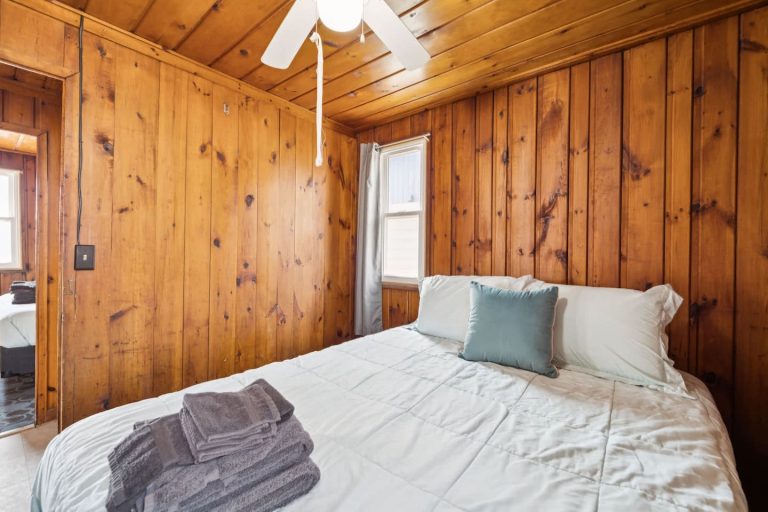 Wood-paneled bedroom with folded towels and doorway Cabin in Oscoda, Michigan — Barefoot Beach Cabin #4, hosted by Roam