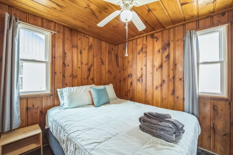 Wood-paneled bedroom with teal accent pillow Cabin in Oscoda, Michigan — Barefoot Beach Cabin #4, hosted by Roam