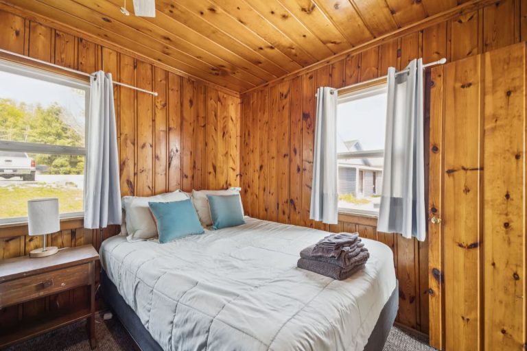 Wood-paneled bedroom with teal pillows Cabin in Oscoda, Michigan — Barefoot Beach Cabin #7, hosted by Roam